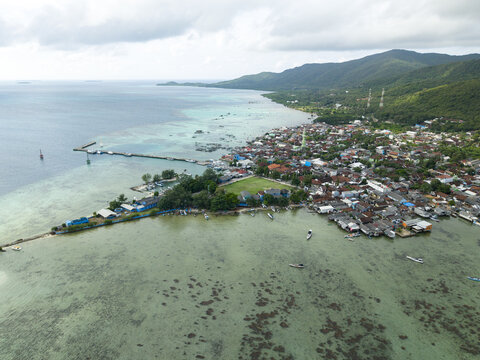 Aerial view of the coastal town where the turquoise sea meets the land with its green vegetation and dense buildings, Karimunjawa, Central Java, Indonesia.