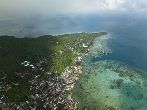 Aerial view of the vibrant coastal settlement meeting the turquoise waters, lush green forests, and distant horizon, Karimunjawa, Central Java, Indonesia.
