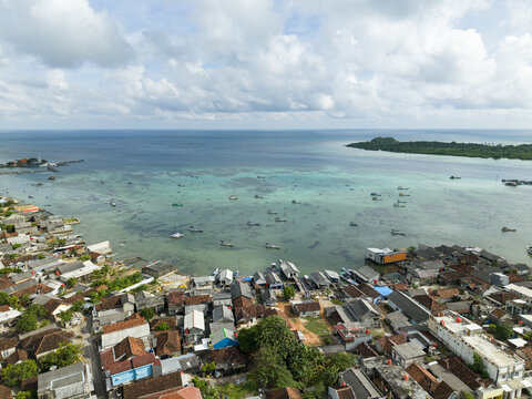 Aerial view of the coastal village where houses meet the turquoise sea, a vibrant contrast under the expansive sky, Karimunjawa, Central Java, Indonesia.