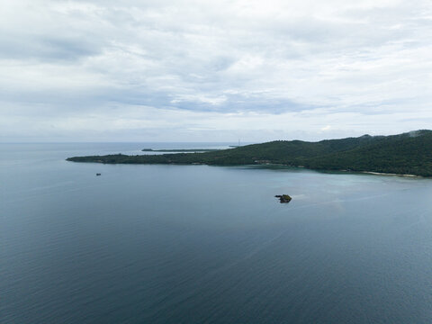 Aerial view of deep blue waters embrace the lush green island under a soft, cloudy sky, Karimunjawa, Central Java, Indonesia.