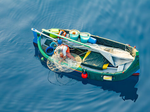 Aerial view of a small, vibrant fishing boat bobs on the tranquil, deep blue sea, its nets and gear scattered about, Ghajnsielem, gozo, Malta.