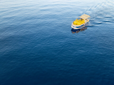 Aerial view of a boat carrying bright yellow objects glides through the deep blue sea, creating a striking contrast of color, Ghajnsielem, Gozo, Malta.