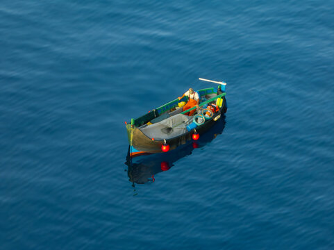 Aerial view of a small boat adrift on the tranquil, sapphire expanse of the sea, its vibrant red buoys standing out against the deep blue waters, Ghajnsielem, gozo, Malta.