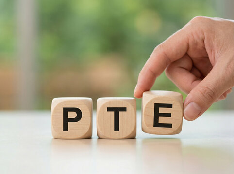 pte wooden cubes with hand placing final letter on reflective surface with soft green blurred background for education concept