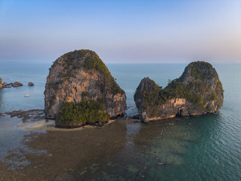 Aerial view of towering limestone cliffs rise majestically from the turquoise waters, their rugged surfaces softened by patches of verdant vegetation, Krabi, Thailand.