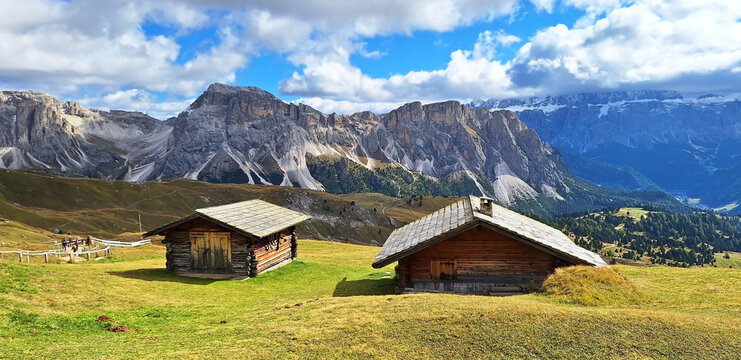Two mountain refuges (wooden houses) stand against the backdrop of the Mastle Hutte and Seceda mountains on a cloudy autumn day. Panorama.