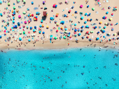 Aerial drone view of colorful umbrellas on sandy beach, swimming people in blue sea on sunny summer day. Top down view. Mallorca, Balearic Islands, Spain. Tropical. Clear turquoise water. Travel