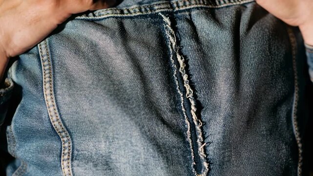 Starting tight grip at seam, hands pulling denim jacket up in studio closeup, revealing frayed seam