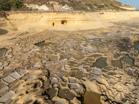 Aerial view of the golden-hued, textured landscape of the Qolla l-Bajda Salt Pans, where geometric pools meet rugged cliffs, Iz-Zebbug, Gozo, Malta.