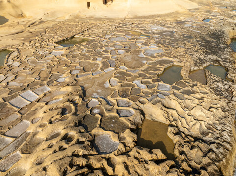 Aerial view of salt pans create a mosaic of light and shadow, the geometric patterns etched into the earth reflecting the sky, Gozo, Malta.