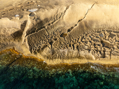 Aerial view of golden cliffs meet the turquoise sea, contrasting textures of rock and water creating a stunning coastal scene, Malta, Malta.