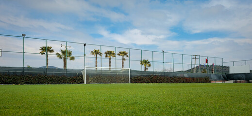 Soccer Goal on Lush Green Field With Palm Trees and Fenced Outdoor Sports Court © ismailbasdas