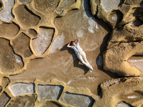 Aerial view of a lone figure basking in the sun amidst the geometric patterns of the Qolla I-Bajda Salt Pans, Iz-Zebbug, Gozo, Malta.