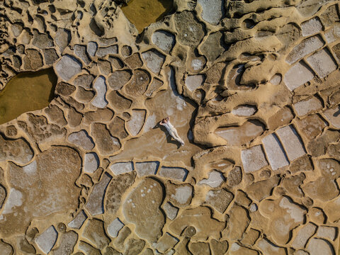 Aerial view of sun-baked salt pans patterned like a mosaic, where a solitary figure rests amidst the geometric landscape, Iz-Zebbug, Gozo, Malta.