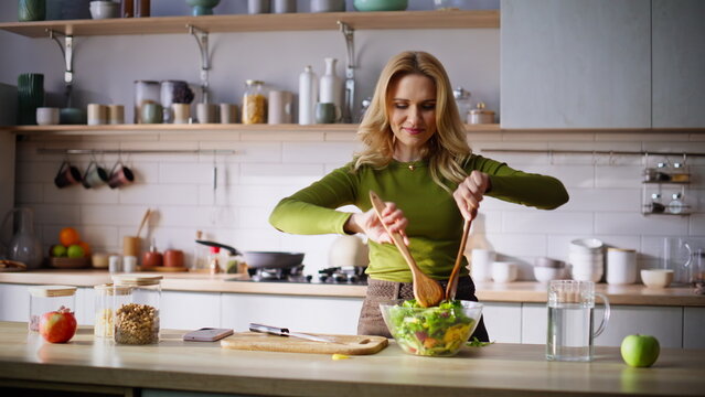 Slim blonde mixing vegetables cooking salad home closeup. Woman sniffing aroma