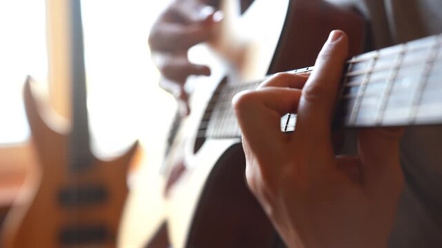 A man is playing a guitar while seated indoors. The guitar music fills the room as a second guitar is visible in the background near the window.