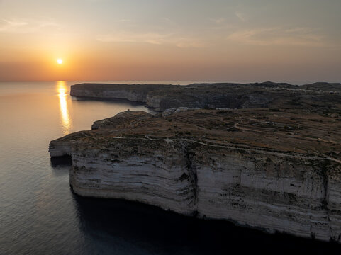 Aerial view of rugged cliffs meet the tranquil, sun-kissed sea, creating a stunning contrast of textures and tones at Sanap Cliffs, Munxar, Gozo, Malta.