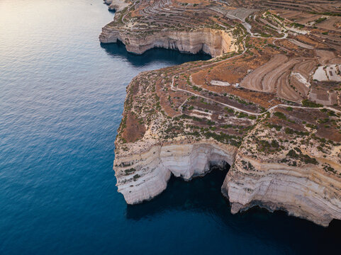 Aerial view of rugged cliffs meeting the deep blue sea at Sanap Cliffs, contrasting with the terraced landscape above, Munxar, Gozo, Malta.