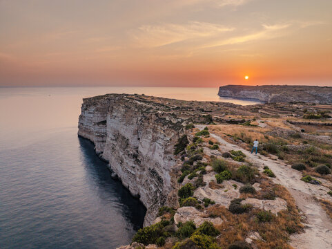 Aerial view of golden sunset paints the sky over the rugged Sanap Cliffs, casting long shadows on the tranquil sea, Munxar, Gozo, Malta.