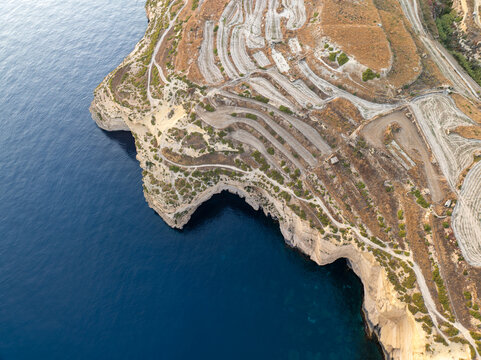 Aerial view of the rugged Sanap Cliffs meeting the deep blue sea, a contrast of arid land and endless ocean, Munxar, Gozo, Malta.