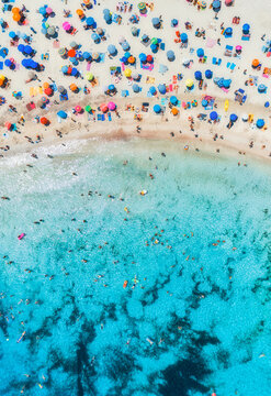 Aerial drone view of colorful umbrellas on sandy beach, swimming people in blue sea on sunny summer day. Top down view. Mallorca, Balearic Islands, Spain. Tropical. Clear turquoise water. Travel