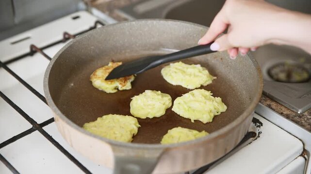 Frying golden zucchini potato pancakes in ceramic skillet on gas stove cooking process