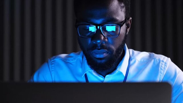 Focused Black Man Working on Laptop in Dark Room