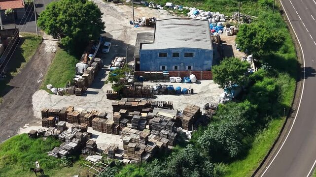 Aerial video footage of a junkyard with a large pile of scrap metal and cars next to a road