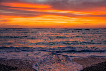 Fototapeta premium Dramatic Golden sunset over tranquil beach, waves lashing the pebble coastline