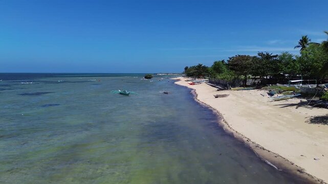 Aerial view of a tropical beach lined with palm trees and clear turquoise water with traditional Bangka boats creating a vibrant coastal scene on Bantayan Island Philippines Southeast Asia