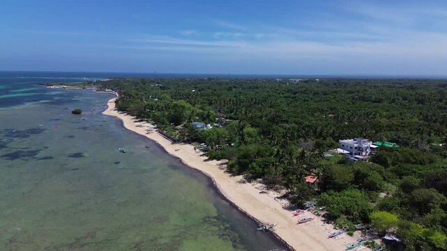 Aerial view of a pristine tropical beach with palm trees and turquoise water surrounded by dense green vegetation creating a peaceful and untouched coastal landscape on Bantayan Island Philippines
