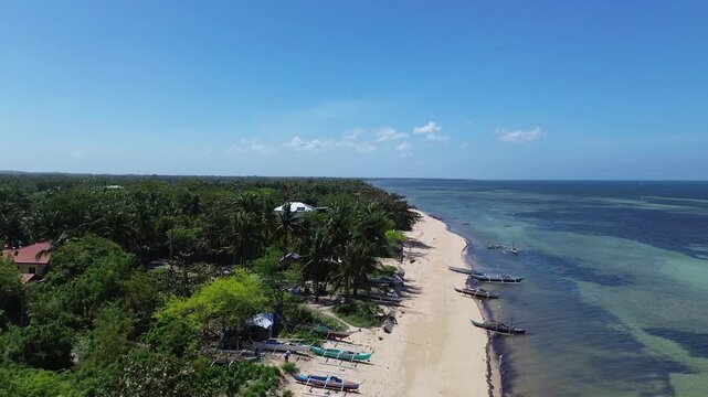 Aerial view of a tropical beach lined with palm trees and clear turquoise water with traditional Bangka boats creating a vibrant coastal scene on Bantayan Island Philippines Southeast Asia
