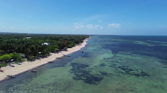 Aerial view of traditional Bangka boats anchored along a tropical shoreline with clear water and sandy beach surrounded by lush green vegetation on Bantayan Island Philippines Southeast Asia