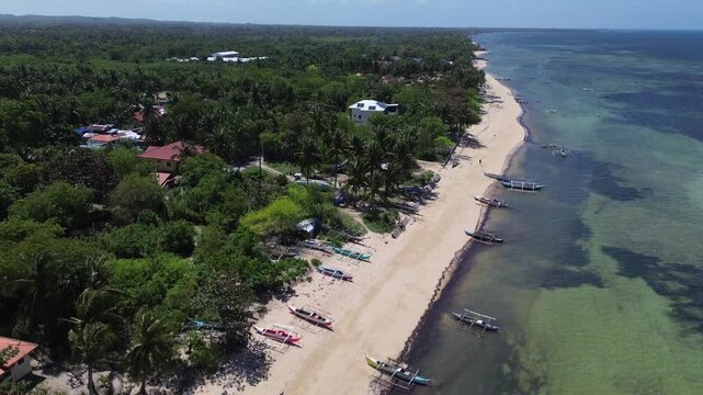 Aerial view of traditional Bangka boats anchored along a tropical shoreline with clear water and sandy beach surrounded by lush green vegetation on Bantayan Island Philippines Southeast Asia