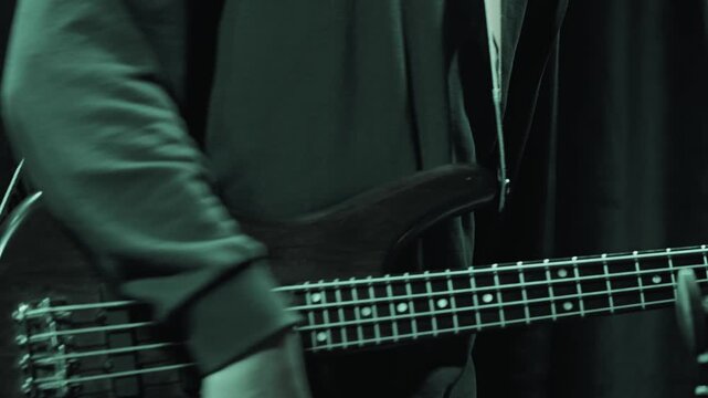A musician plays bass guitar on stage. Close-up on hands and fretboard under dramatic purple and magenta lighting. Energetic, moody atmosphere of a rock concert or live music event