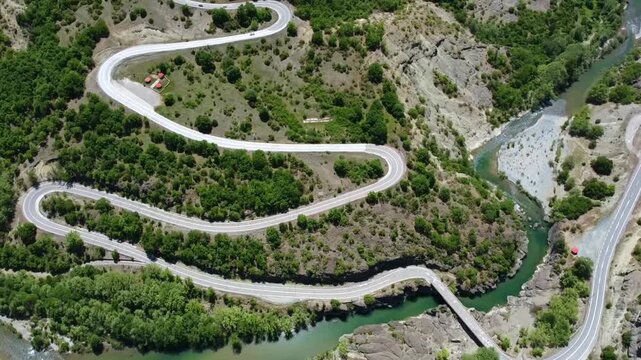 Cinematic drone shot of an epic winding road passing through a rugged canyon. High-angle view of the zig-zag route and the turquoise river below. Ideal for adventure travel and road trip storytelling.