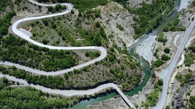Cinematic top-down drone shot of the Venetikos river gorge. High-angle abstract view of the winding road patterns and the turquoise water flowing through the canyon. Unique infrastructure geometry.