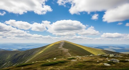 A majestic green mountain ridge stretches under a bright blue sky with fluffy white clouds and distant hazy valleys.