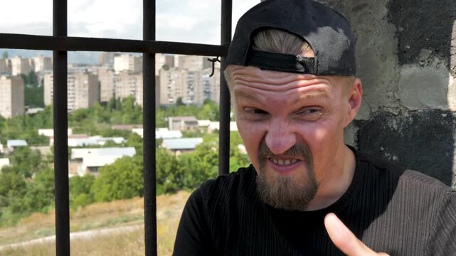 Criminal sitting in prison making threatening gesture by drawing finger across throat. Threat from recidivist offender. Convicted prisoner with cap and beard. Unrepentant for crime