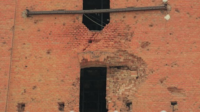 Close up of a war-torn red brick wall. Bullet holes shrapnel damage scar the surface of the ruined building, evoking a somber, historic mood. The Gerhardt Mill