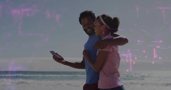 Couple walking arm-in-arm on beach, man tilting phone, magenta overlay growing over scene for tech
