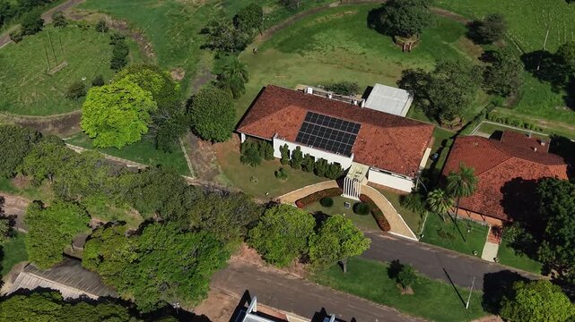 Aerial video of a large house with solar panels on the roof surrounded by trees and greenery