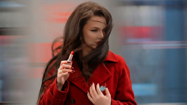 Elegant brunette with red lipstick trying to fix makeup as train wind ruins her hair