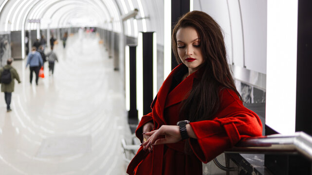 A stylish brunette in a red coat waiting for a train in the subway