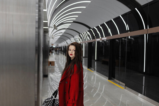 A stylish brunette in a red coat waiting for a train in the subway