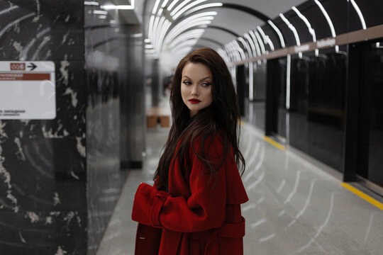 A dark-haired woman in a crimson coat on a metro platform, rushing for business