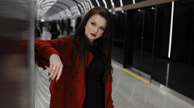 A stylish brunette in a red coat rushing on a subway platform, city life