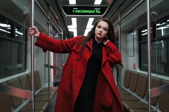 A beautiful brunette in an alizarin red coat riding the metro, urban street fashion