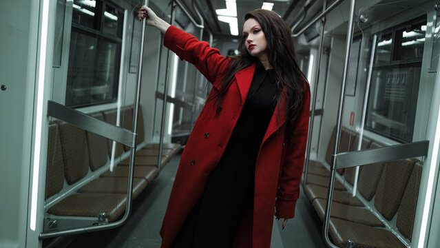 An elegant brunette in a crimson coat riding the metro, city life and street fashion