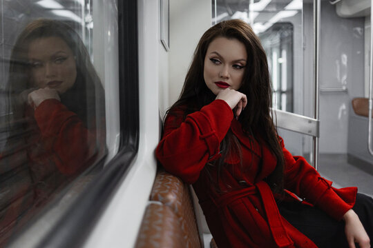 A stylish brunette in a scarlet coat riding a subway car, city rhythm